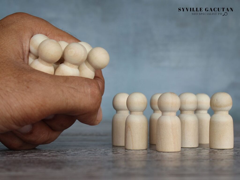Hand gripping wooden figures with a group of figures in the background.