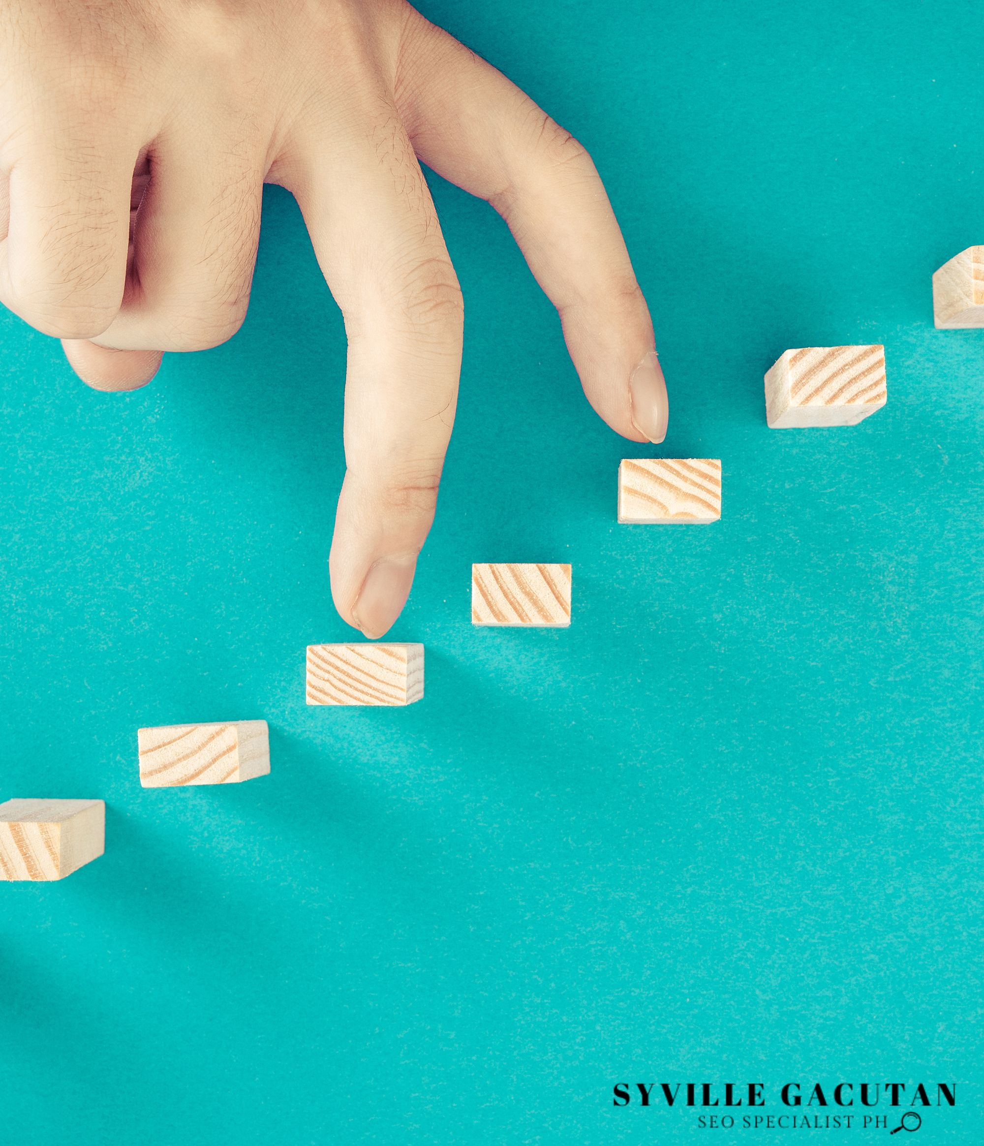 Hand stepping on wooden blocks as stairs against a teal background.