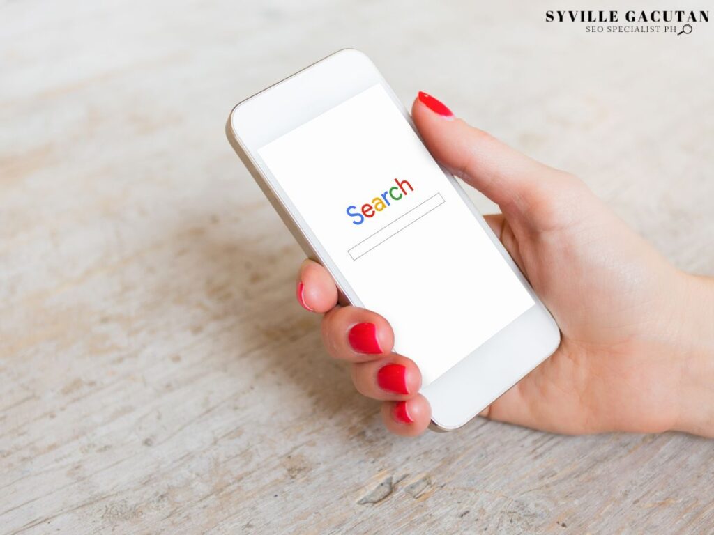 A hand holding a phone with the word "Search" on the screen.
