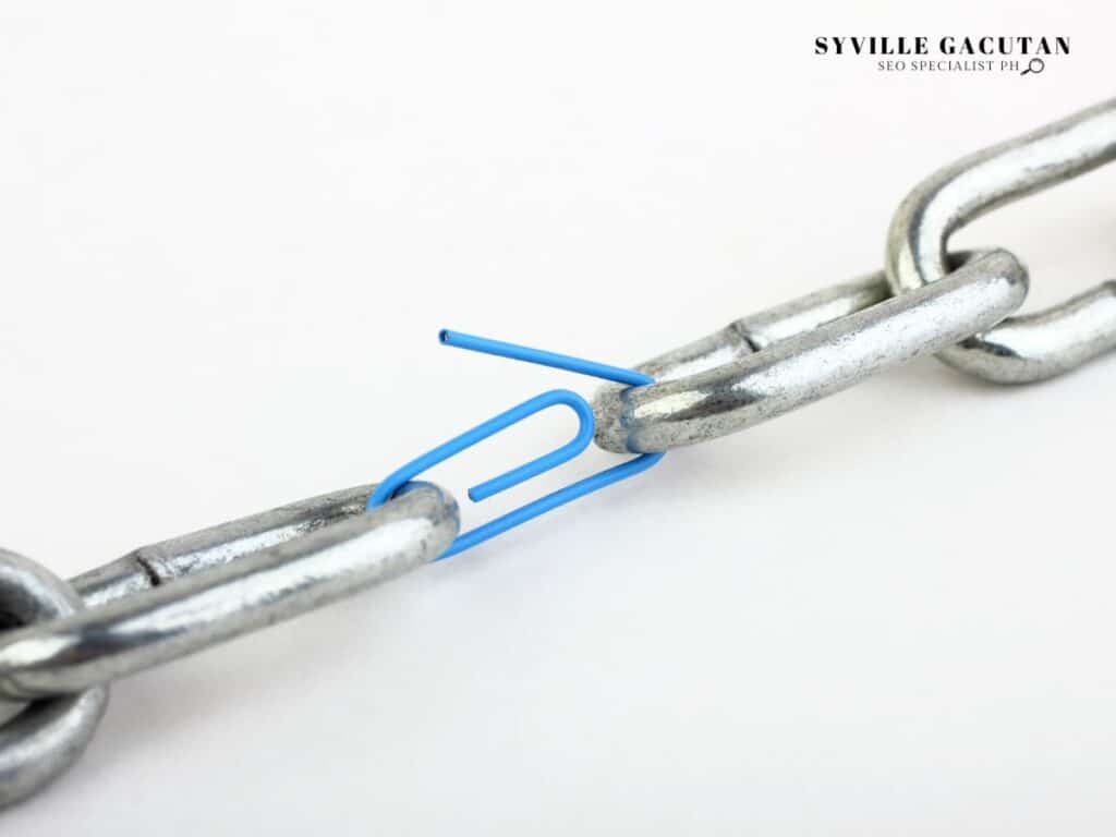 A blue paperclip holding together two metal chain links.