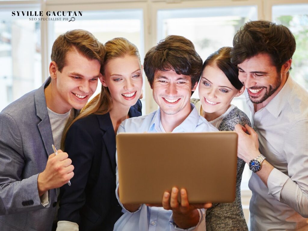 Group of five people smiling at a laptop screen.