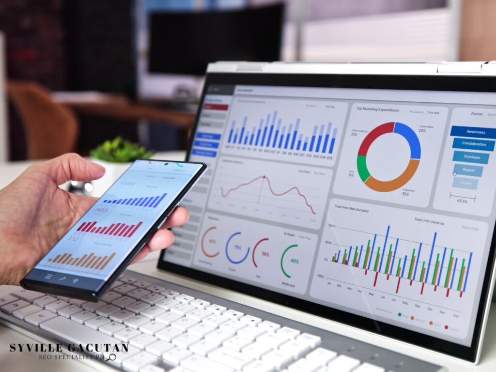 Hand holding smartphone with analytics on screen and laptop nearby.