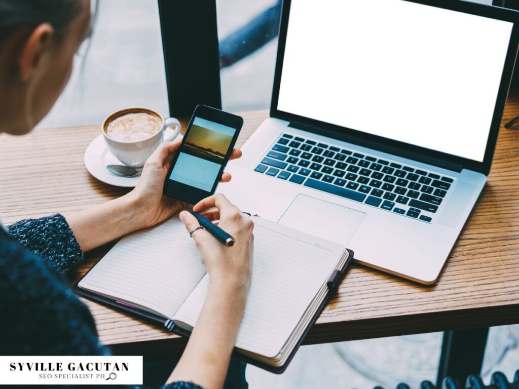 A woman with her laptop taking down notes while holding her phone.
