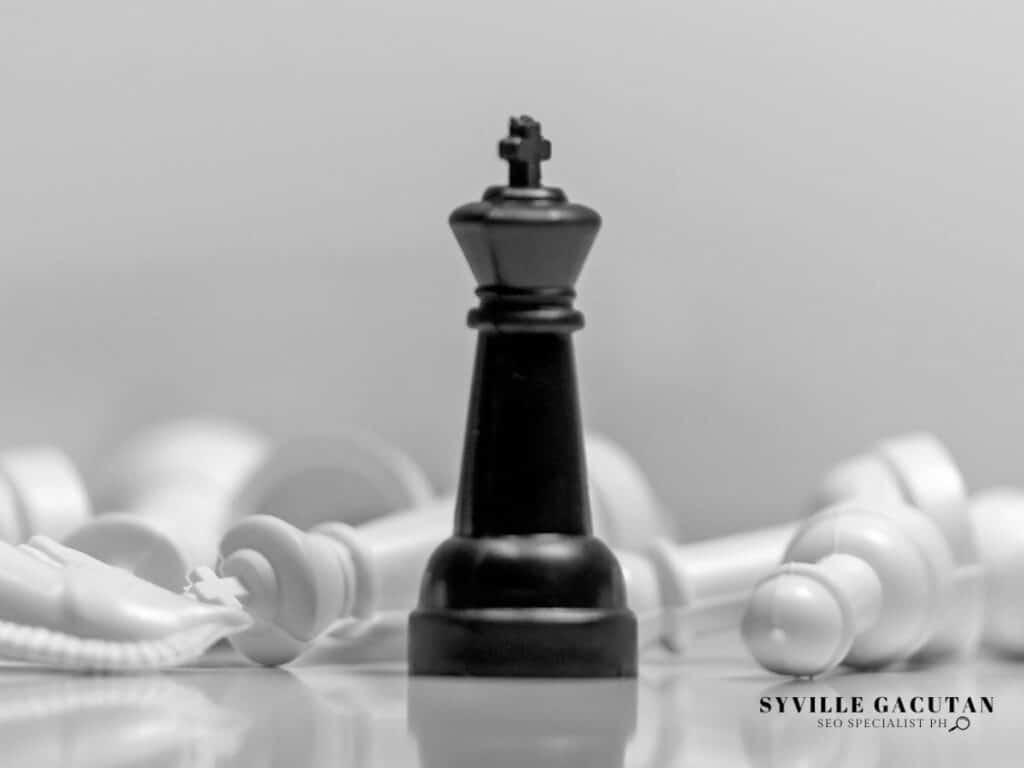 A black chess king stands tall, with fallen white pieces in the background.


