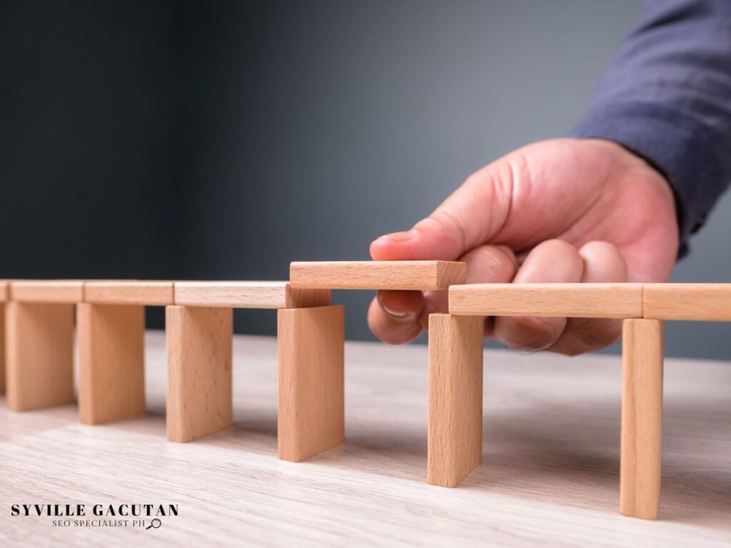 Hand placing a wooden block to complete a gap in a bridge structure.