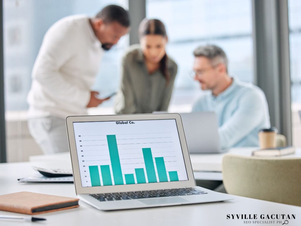 A laptop displaying graphs on the screen with the employees in the background.