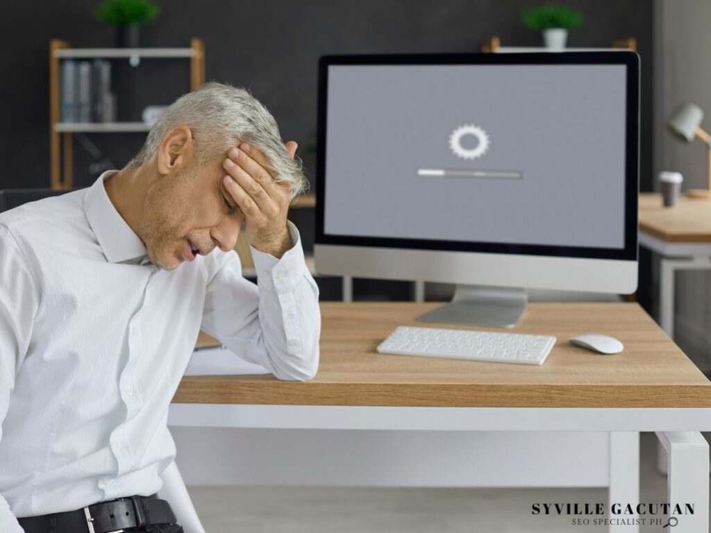 Frustrated man with head in hand, waiting for a loading screen on his computer.