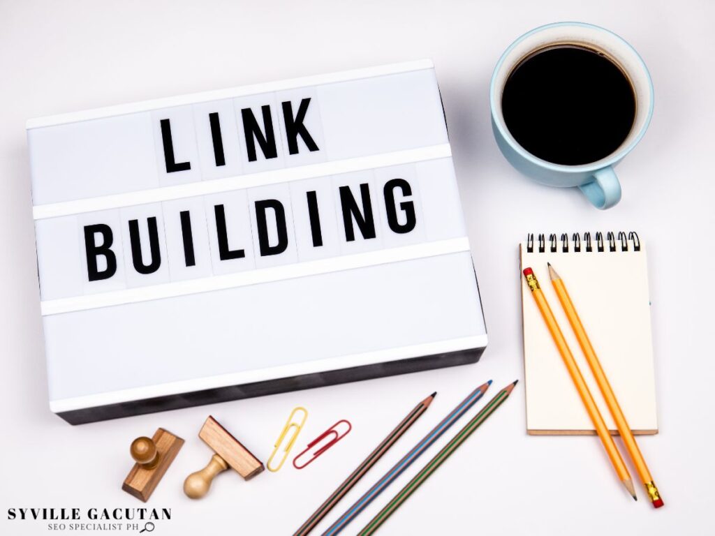 A word "LINK BUILDING" on small board with pencils and coffee beside it.