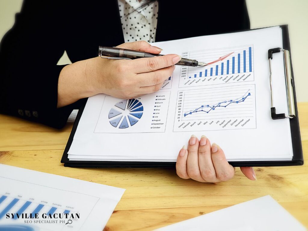 Hand pointing at graphs and charts on a clipboard.