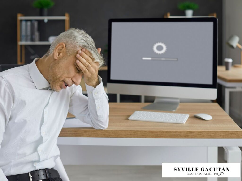 Frustrated man holding head, looking at a loading screen on his desktop.