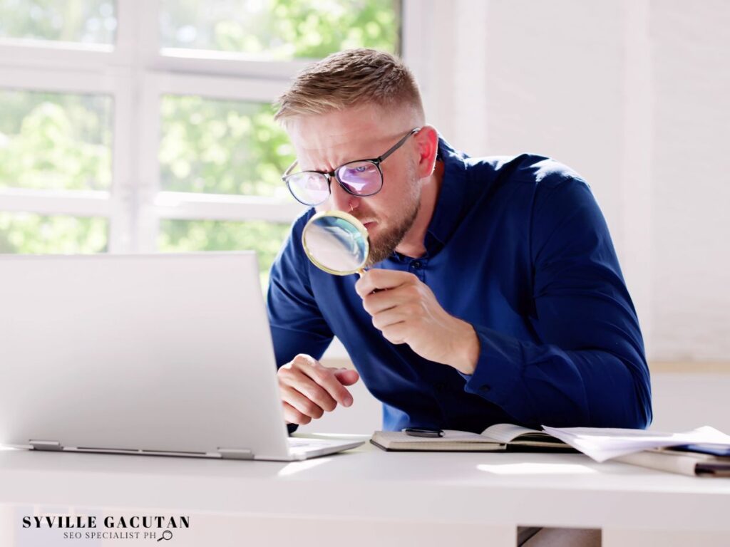 A man using a magnifying glass to look at his laptop.