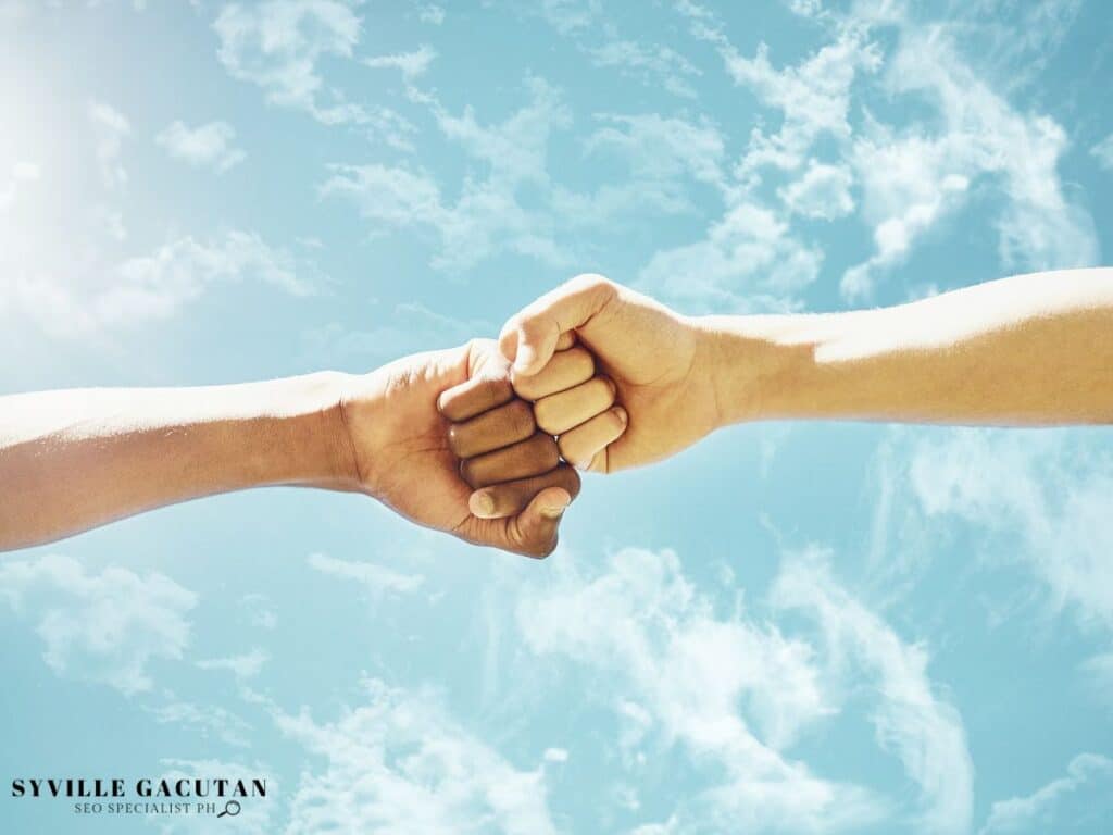 Two hands fists bumping together against a bright sky background.