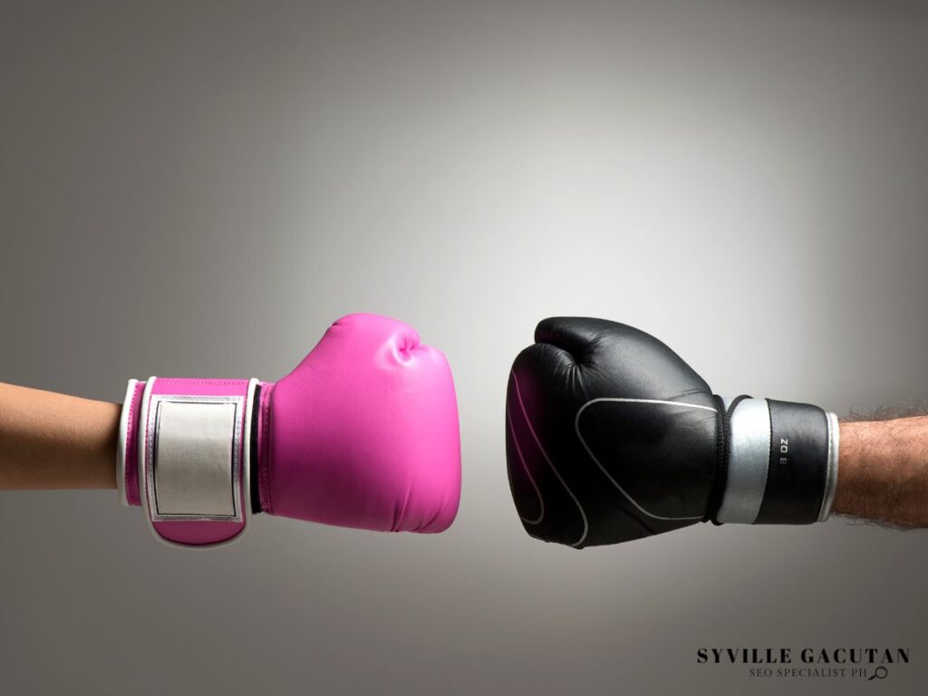 Two boxing gloves, one pink and one black, about to collide.