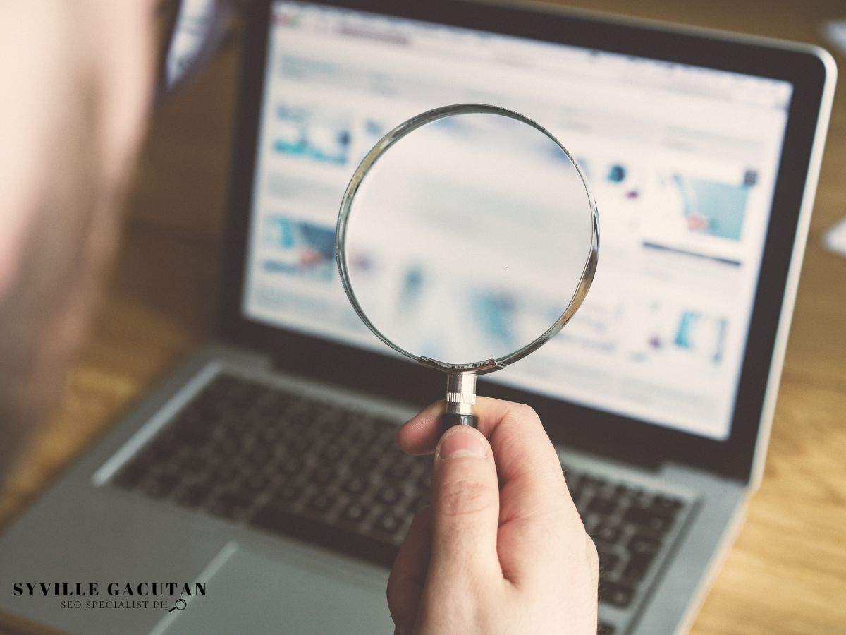 Magnifying glass held in front of a laptop screen displaying a webpage.