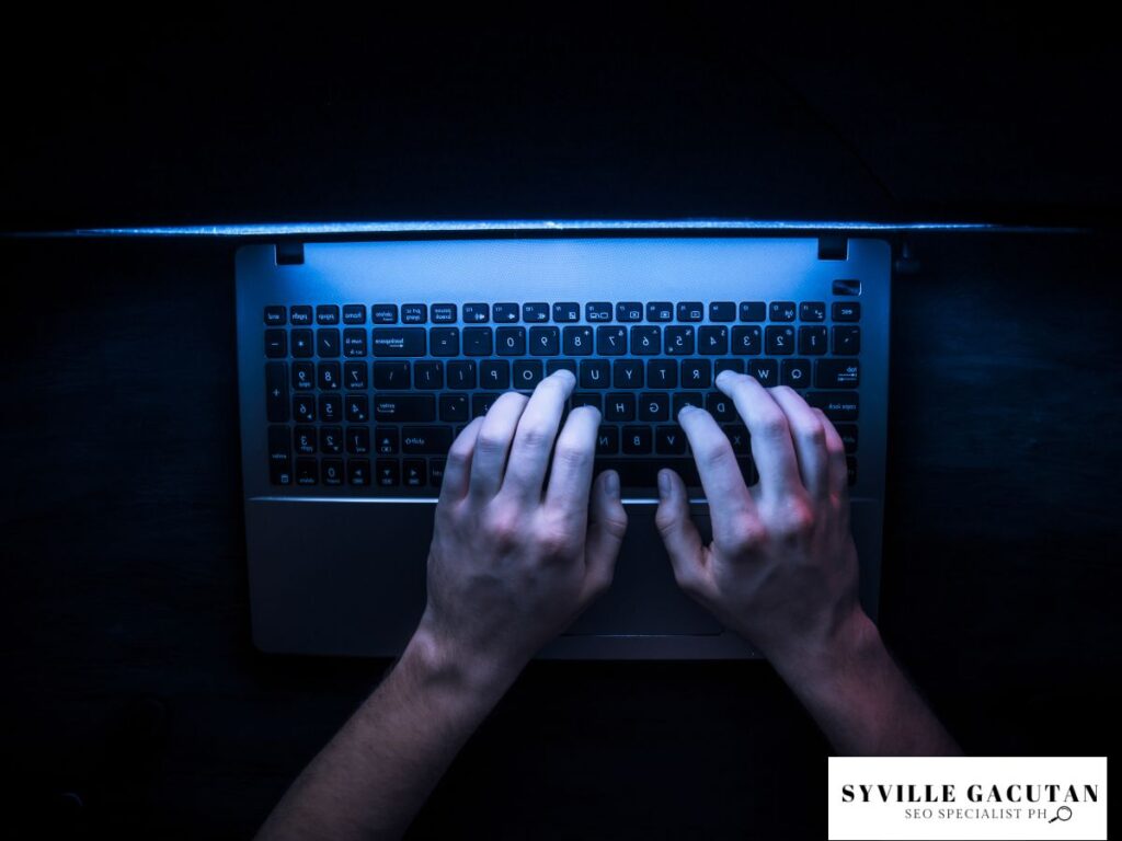 Hands typing on a laptop keyboard in a dimly lit setting.