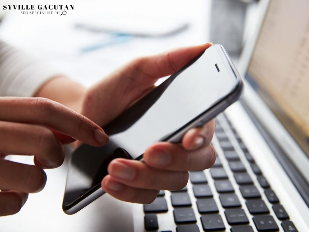 A close-up of a person holding a phone while using a laptop.