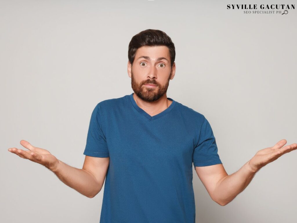 A man in a blue shirt shrugging with a confused expression.