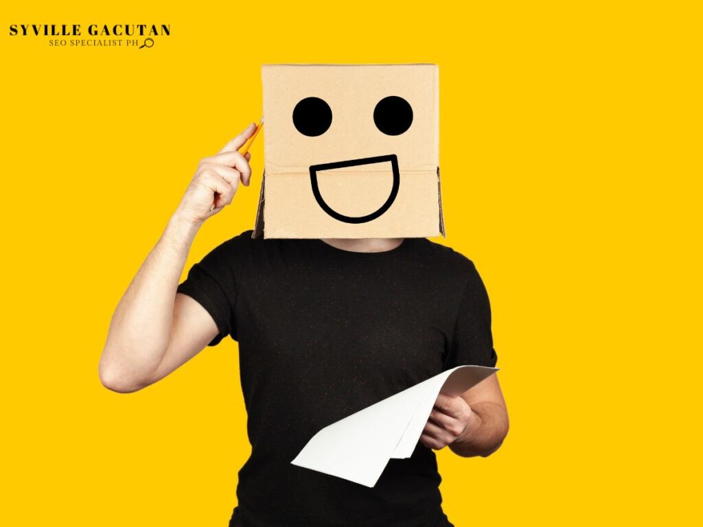 A person wearing a box with a smiling face drawn on it, holding a paper, in a yellow background.