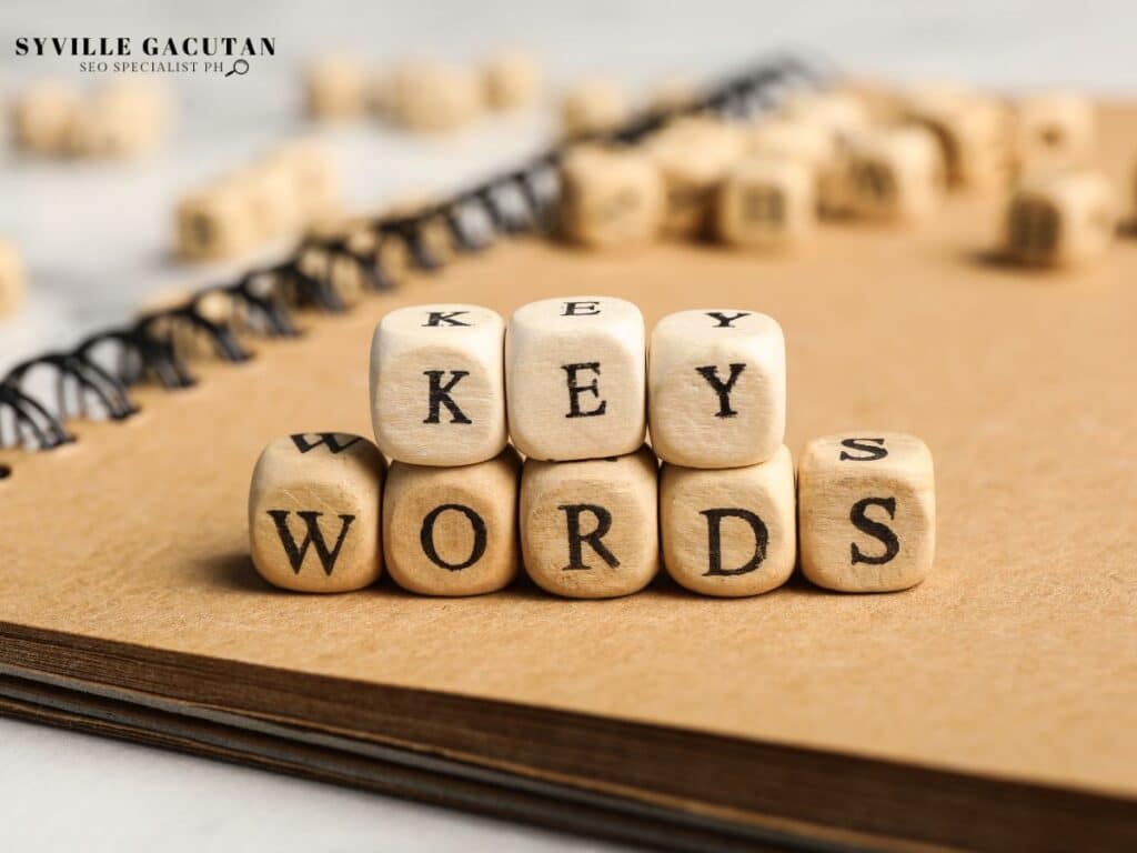 Wooden cubes spelling out "KEYWORDS" stacked on a notebook.