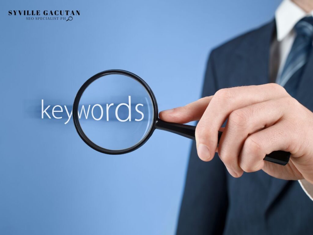 A hand holding a magnifying glass over the word "keywords" on a blue background.