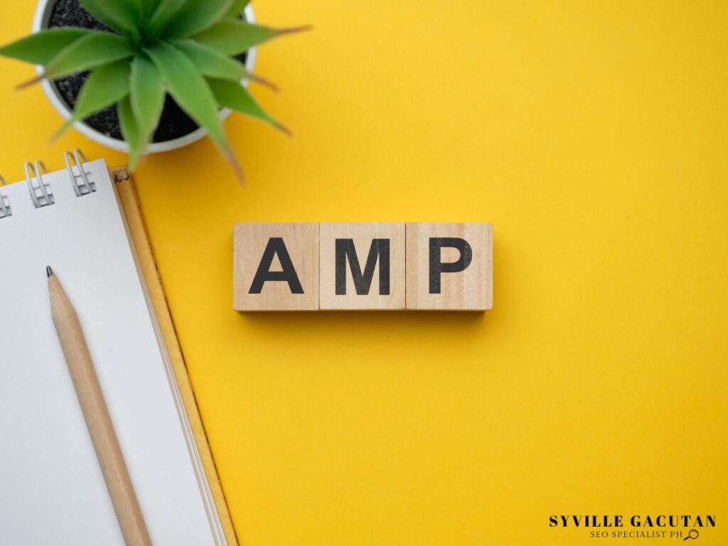 Wooden blocks spelling "AMP" next to a plant and notebook.