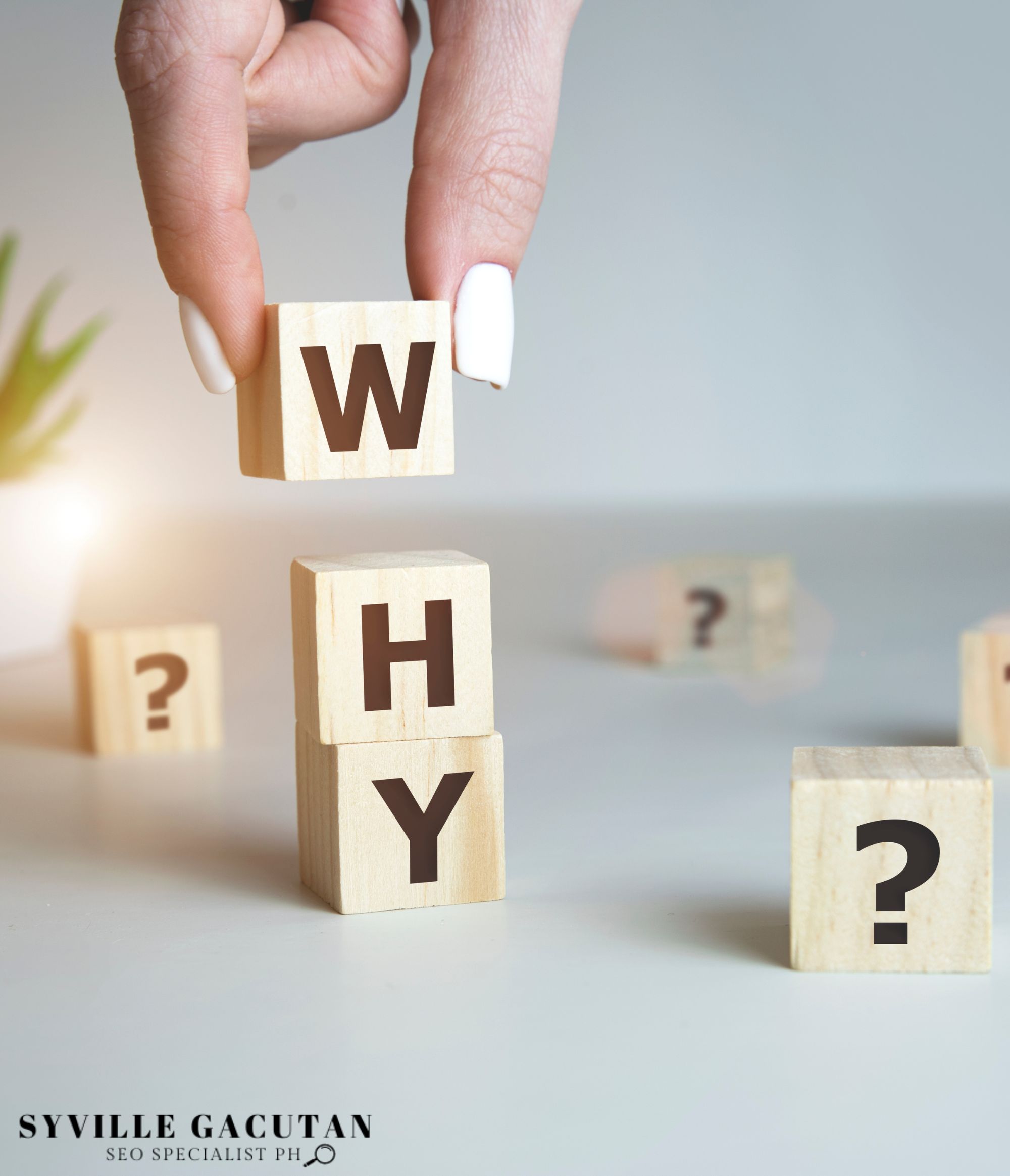 A hand stacking a wooden blocks that spells "WHY"