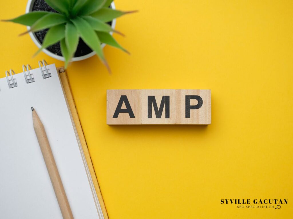 Wooden blocks spelling "AMP" on a yellow background near a notebook and pencil.