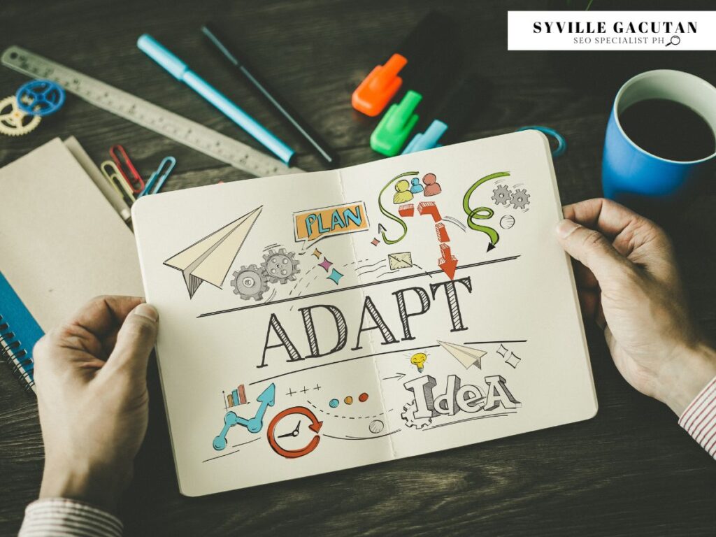 Notebook sketch showing "ADAPT" concept with icons, arrows, and planning elements on wooden desk.