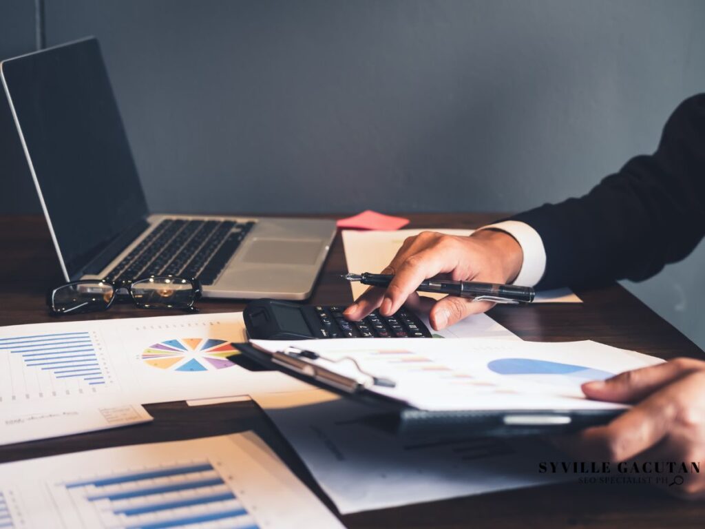 Businessman using a calculator with charts and graphs on the table.