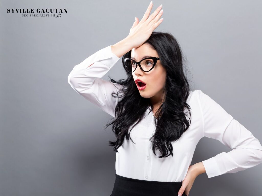 A woman in business attire with glasses showing surprise expression against gray backdrop.