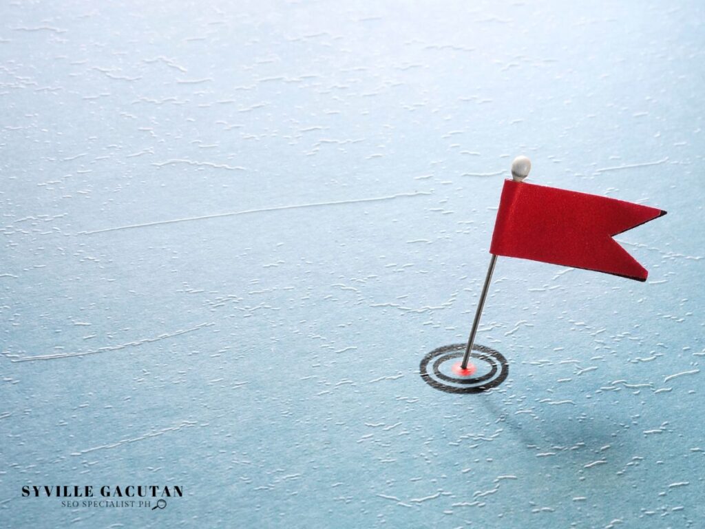 Red flag planted on a bullseye target against light blue textured background.