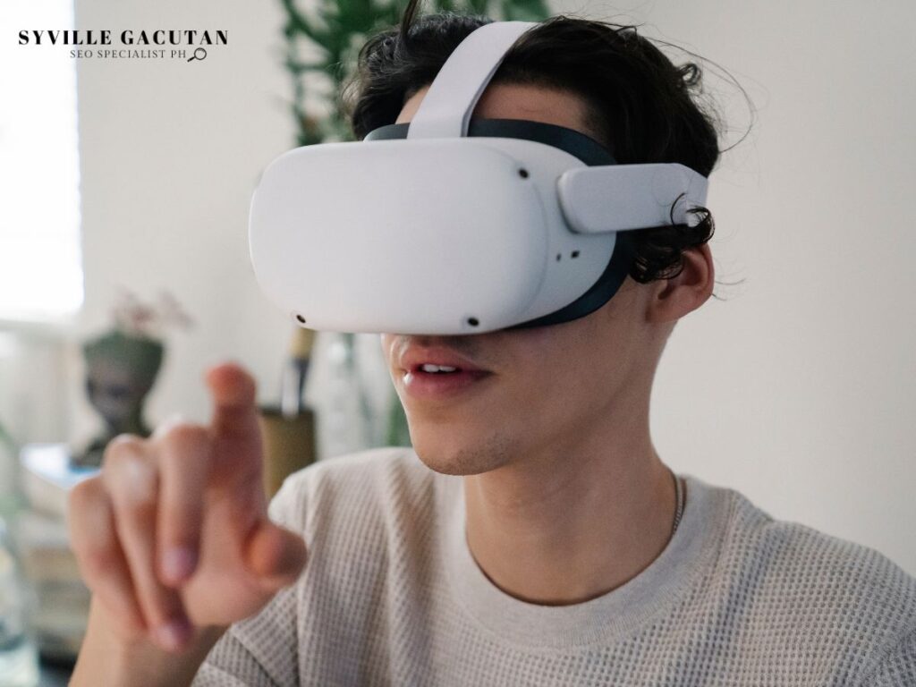 Person wearing white VR headset in cream sweater, gesturing with hand against light background.