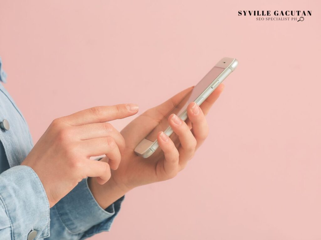 Person using a smartphone on a soft pink background.