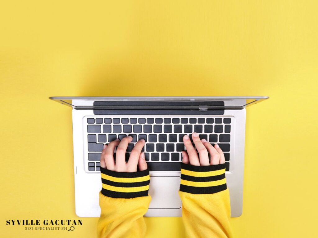 Hands typing on a laptop with a vibrant yellow background.
