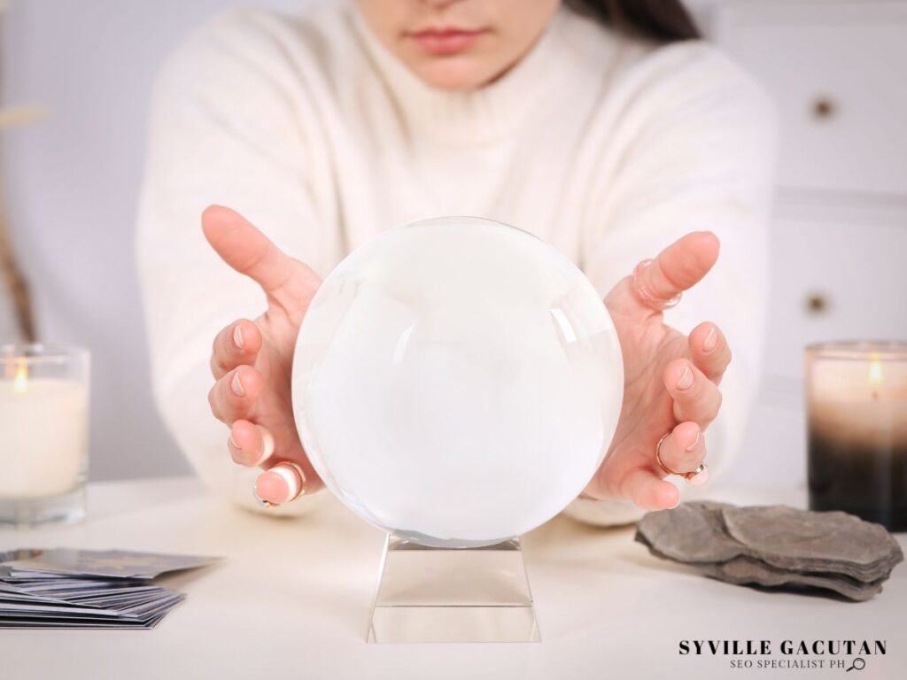 Woman holding a crystal ball on a table with candles, cards, and stones.