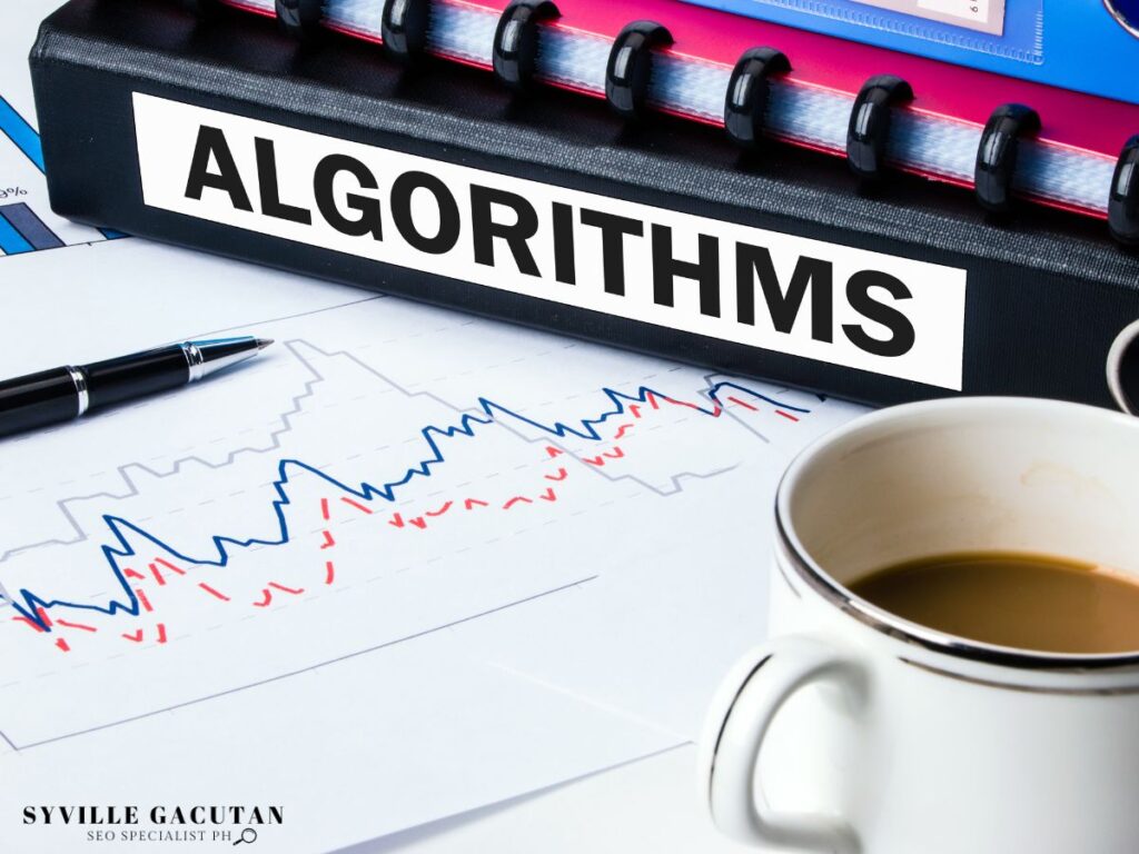 Office desk with "ALGORITHMS" binder, graph charts, and coffee cup showing data analysis setup.