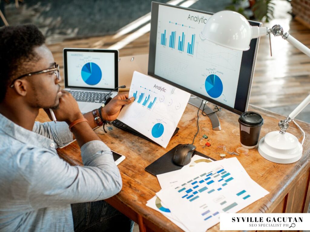 Man analyzing printed charts at a desk with a computer setup.