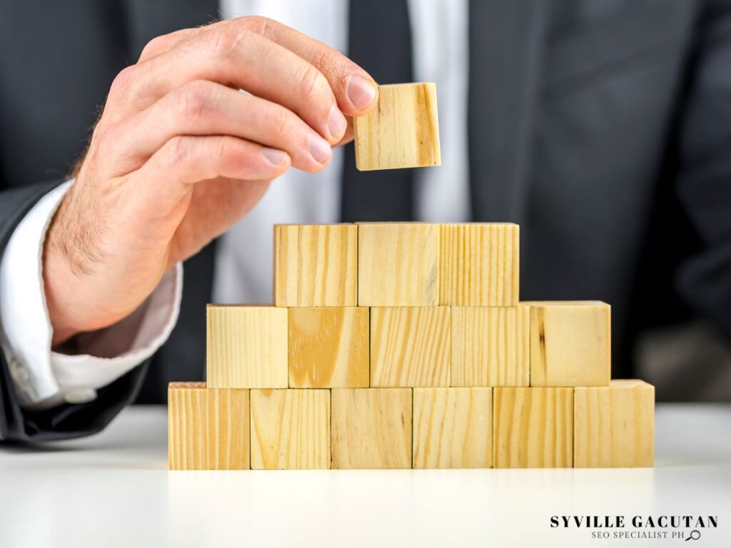 Hand placing wooden block on pyramid structure, showing business growth concept.