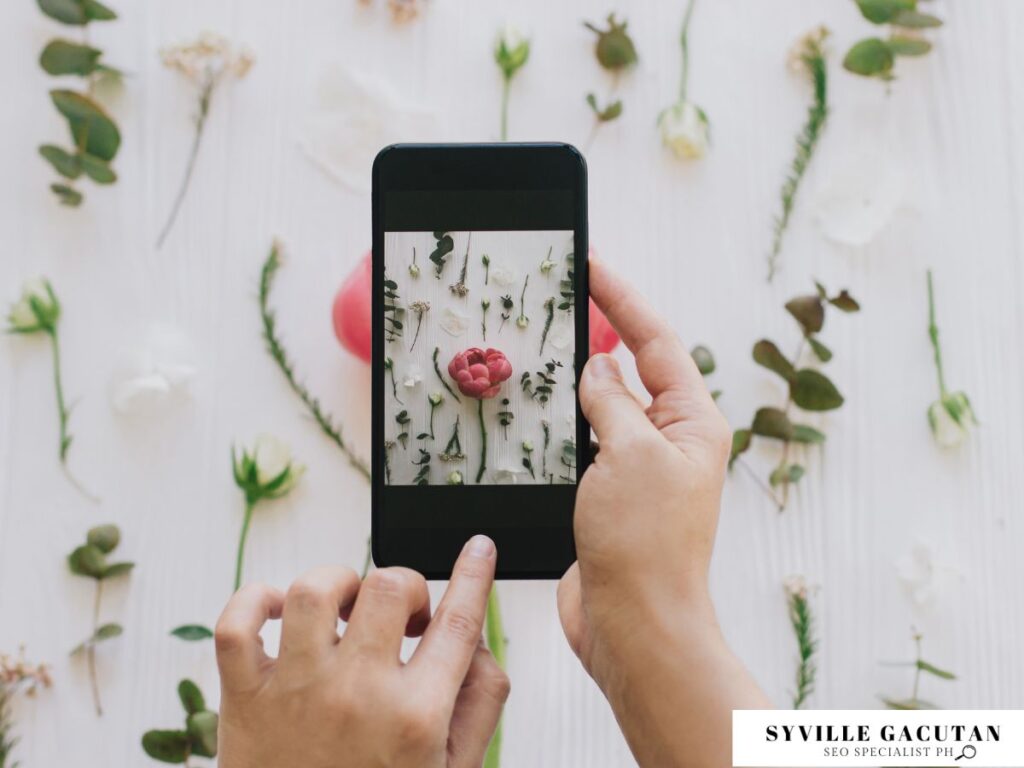 Person photographing flowers arranged neatly on a white background.