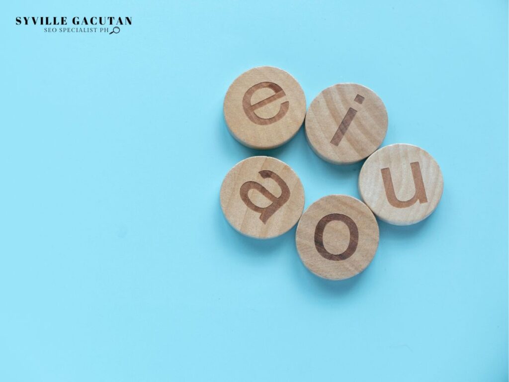 Wooden circular tokens with vowel letters on it against light blue surface.