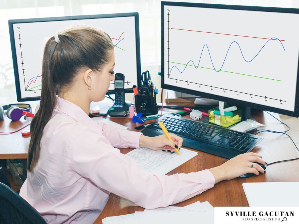 Professional analyzing data trends on dual monitors, taking notes at organized desk workspace.