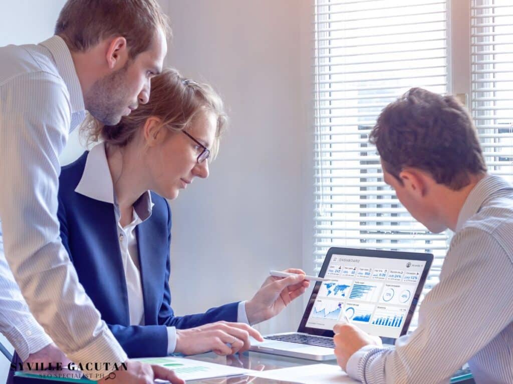 Three people analyzing dashboard data on a laptop.