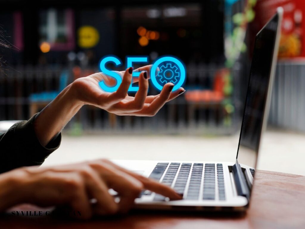 Hand holding a glowing "SEO" hologram above a laptop.