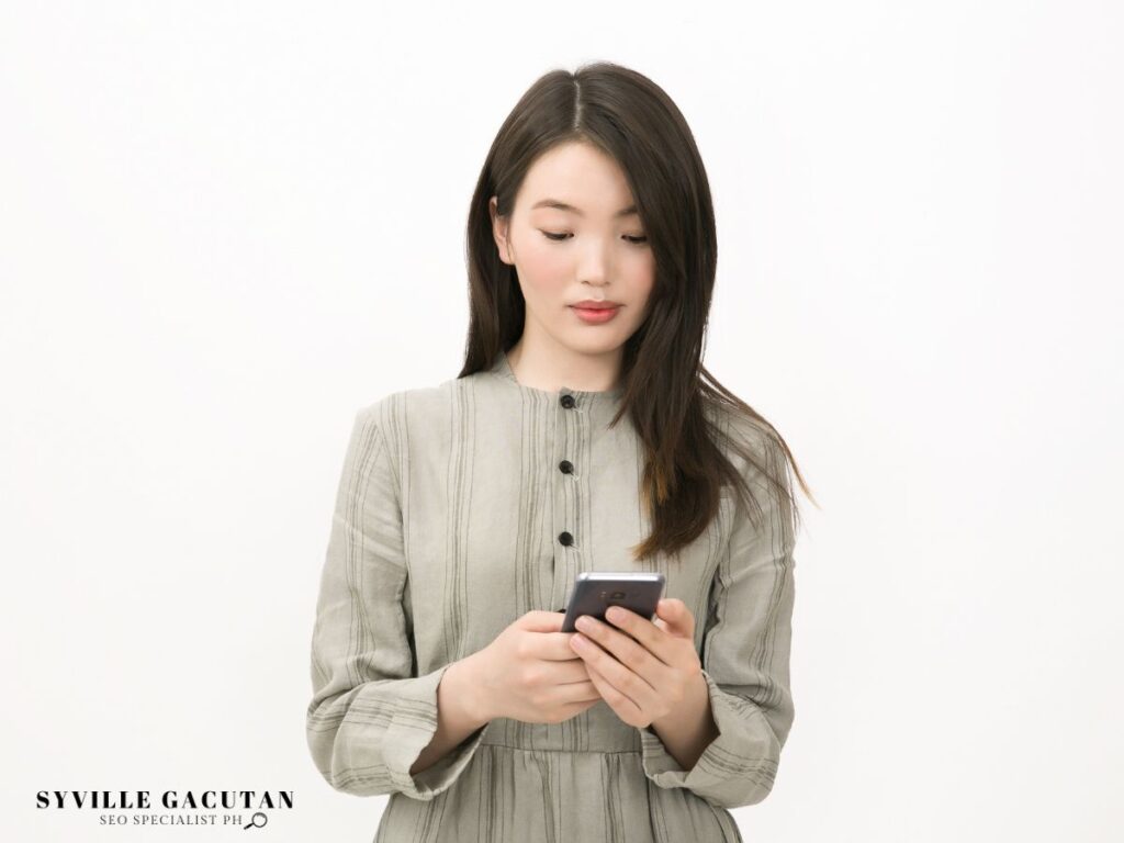 Professional in grey dress using smartphone against white backdrop.