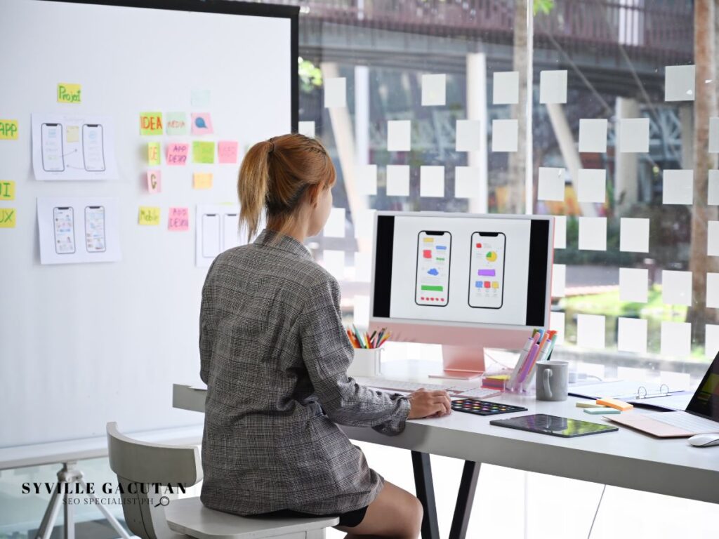 Designer reviewing app layouts on a desktop, surrounded by sticky notes.