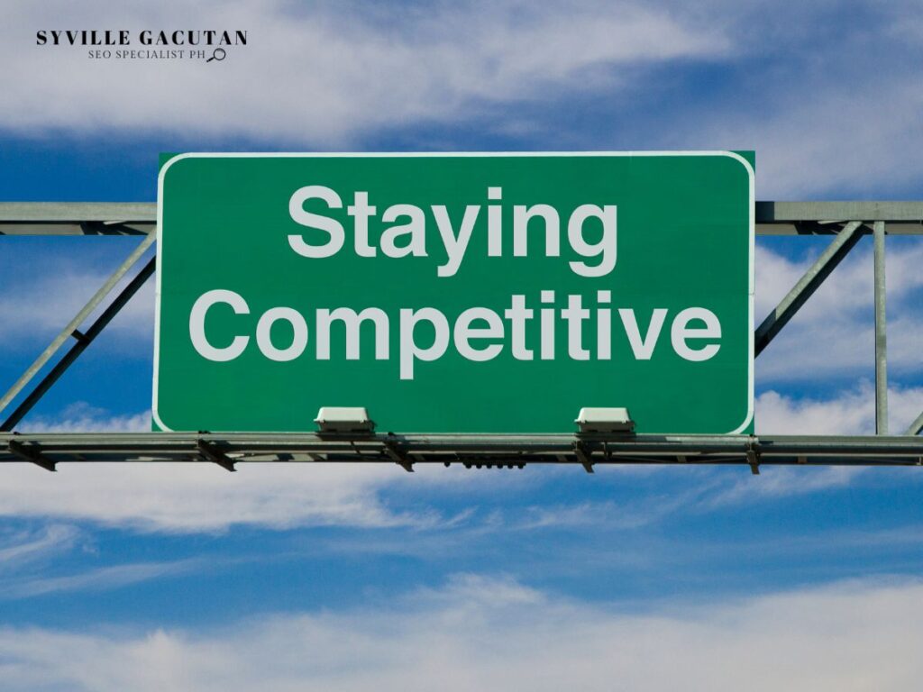 Green road sign with the text "Staying Competitive" against a blue sky.