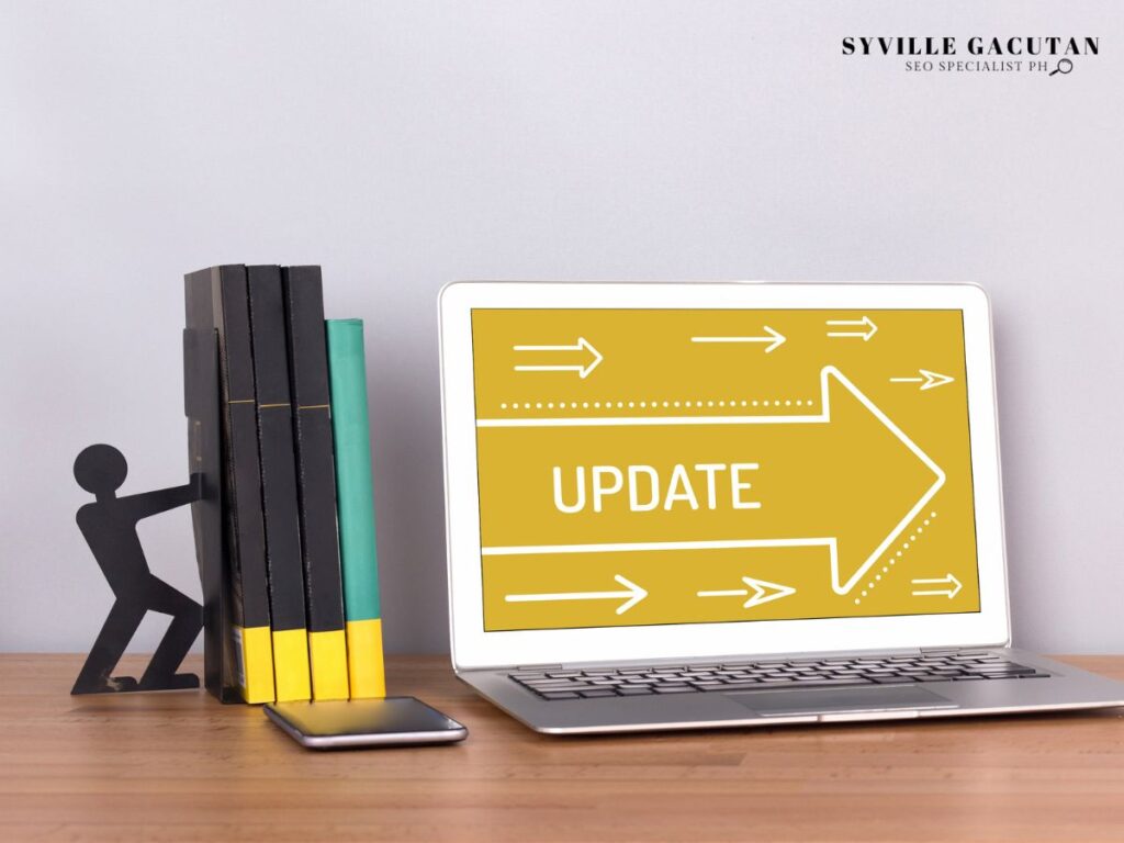 Laptop displaying "UPDATE" in yellow with arrows, books and stick figure bookend on wooden desk.