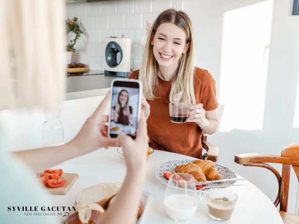 Woman taking a photo of a friend enjoying breakfast.
