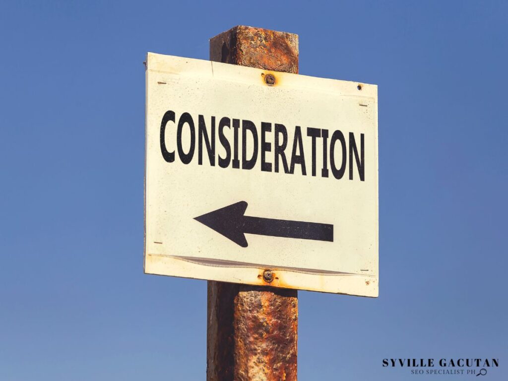 White directional sign with "CONSIDERATION" text and arrow pointing left on rusty metal pole.