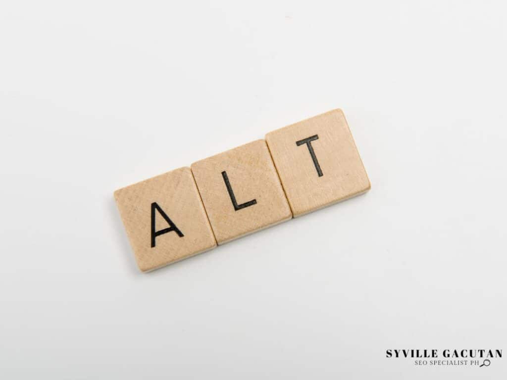 Wooden Scrabble tiles spelling out "ALT" on a white background.